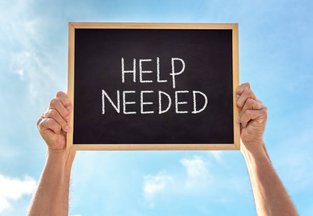 Help needed blackboard sign held up by man against blue sky background